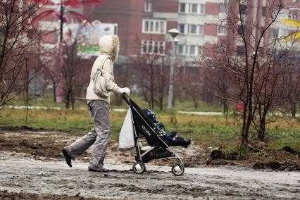 Женщина с ребенком в детской коляске идет по парку.
