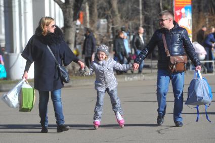 ВВЦ. ВДНХ. Семья с ребенком на роликовых коньках идут по парку.