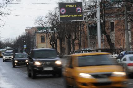 Дорожное табло `Будьте внимательны`. Автомобили с включенными фарами.