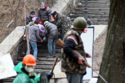 Протестующий с оружием в руках наблюдает за эвакуацией раненного.