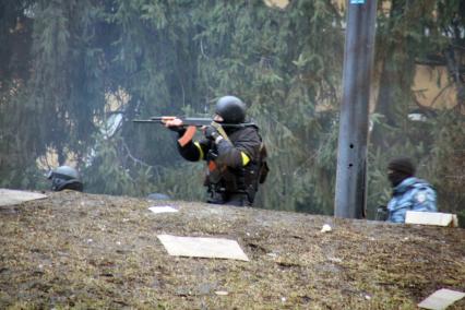 Мужчина в черной военной форме с желтыми повязками на руках с автоматом калашникова.