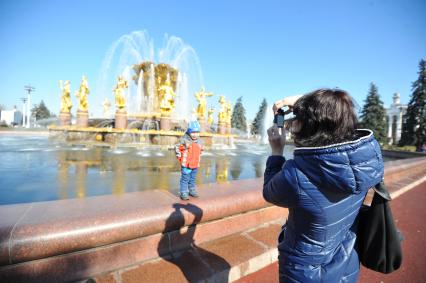 ВВЦ. На снимке: женщина фотографирует ребенка на фоне фонтана `Дружба народов`