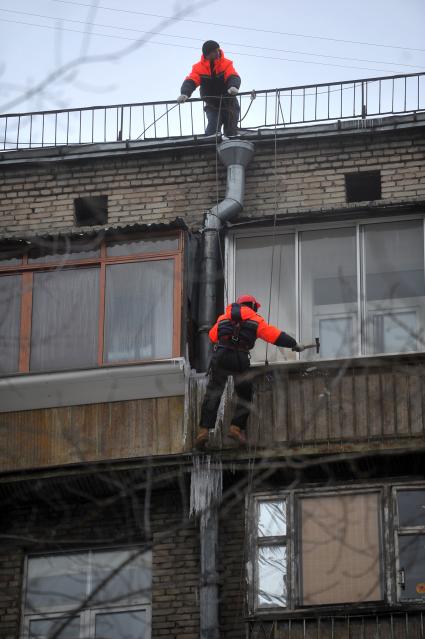 Мужчина сбивает сосульки с фасада здания.