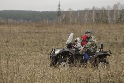 Мужчина и два ребнка едут на квадроцикле по полю