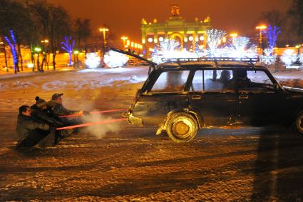 Молодые люди по льду  катаются на веревке, привязанной к заднему бамперу автомобиля.