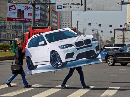 Люди несут плакат с нарисованным автомобилем.