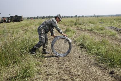 Китайский военный перекатывает колючую  проволоку  во время проведения Российско-Китайских учений Мирная миссия 2013 на полигоне в Чебаркуле