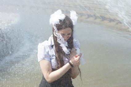 Выпускница с телефоном стояи под струями воды в фонтане во время празднования последнего звонка