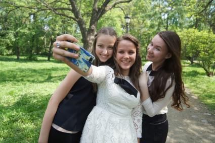 Выпускницы в парке фотографируются на телефон во время празднования последнего звонка в школах