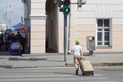 Мальчик везет чемодан через пешеходный переходу