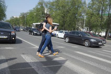 Влюбленная пара обнявшись переходят дорогу по пешеходному переходу