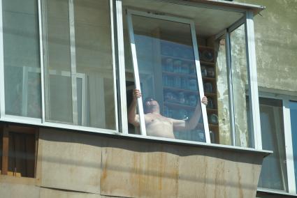Мужчина стоя на балконе устанавливает оконную раму