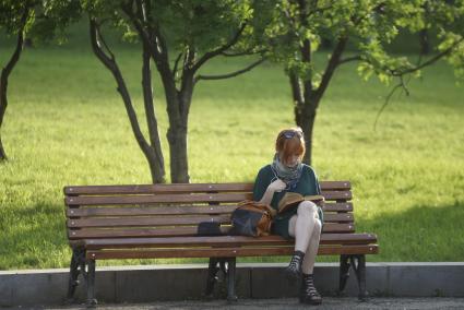 девушка читает книгу сидя на скамейке в парке
