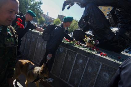 мужчина в зеленом берете с собакой (немецкая овчарка) возлагает цветы к памятнику \"черный тюльпан\" во время дня пограничника