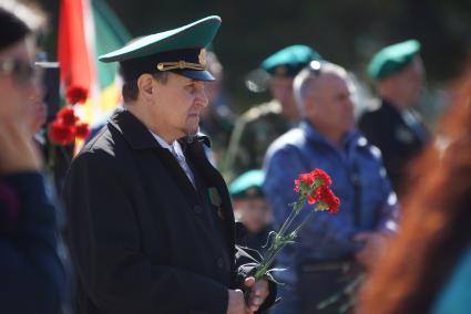 Мужчина в плаще и в зеленой фуражке держит гвоздики во время празднования дня пограничника