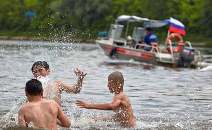 Дети играют в воде на фоне проходящего спасательного катера.