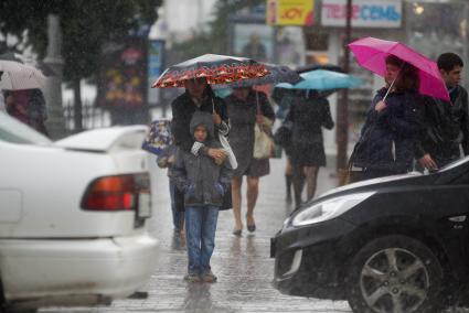 Женщина обняв сына стоят под зонтом на перекрестке во время дождя
