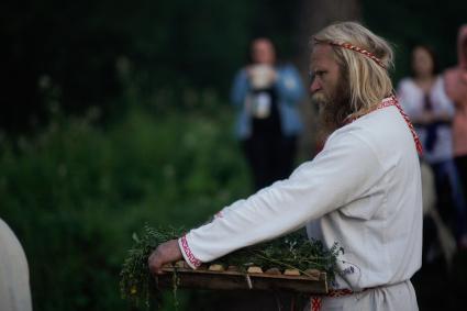 Участник празднования дня Ивана Купала стоит с венком в руках, перед его спуском на воду