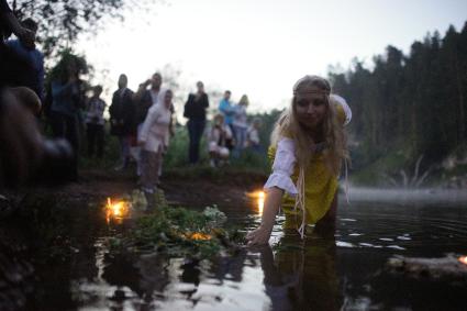 Участница празднования дня Ивана Купала спускает на воду венок