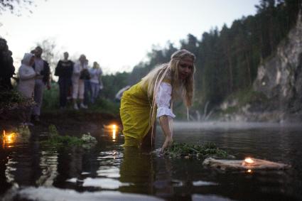 Участница празднования дня Ивана Купала спускает на воду венок