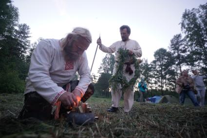 Мужчина с холщевой славянской рубахе разводит огонь в чугунном горшке на празднованиях дня Ивана Купала