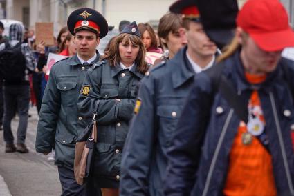 девушка-полицейский в куртке не по росту и с сумочкой идет в оцеплении