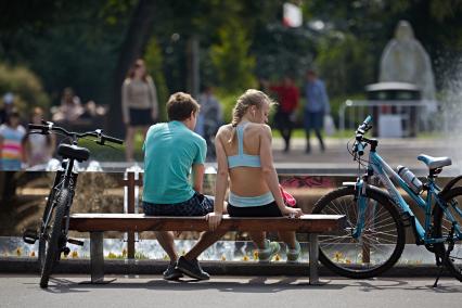 Юноша с девушкой сидят на лавочке, рядом стоят велосипеды.