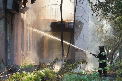 Пожарный из брандспойта тушит огонь в доме