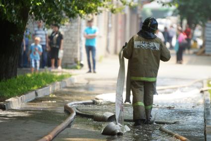 Пожарный идет по тротуару залитому водой от тушения пожара дом в Екатеринбурге