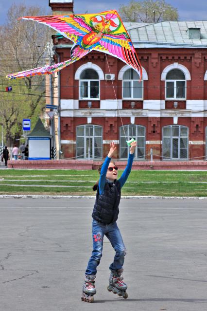 Ребенок пускает воздушного змея катаясь на роликах.