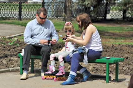 Семья на скамейке в парке экипирует девочку для катания на роликах.