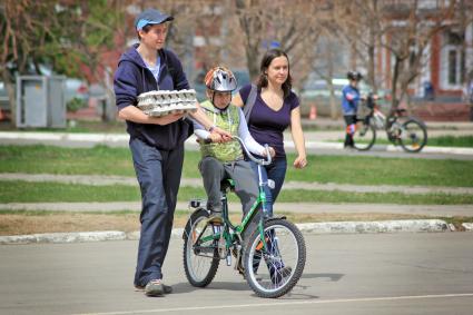 Семья учит ребенка кататься на велосипеде.