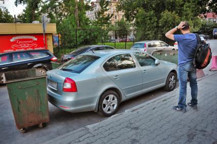 Водитель смотрит на свой автомобиль, `закрытый` двумя мусорными контейнерами.