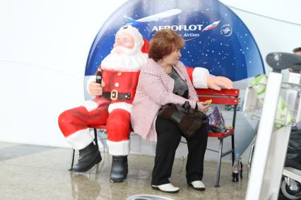 Транспортный коллапс в аэропорту  Шереметьево-2. На снимке: пассажирка сидит на скамье рядом со скульптурой Деда Мороза на фоне баннера `Аэрофлот`.