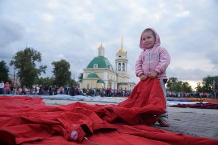 маленькачя девочка держит за край оболочку воздушного шара перед его наполнением на фестиале воздухоплавания \"небо на ладони\"  в Каменске-Уральском