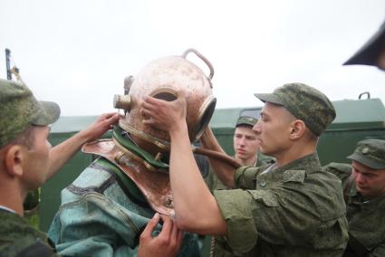 Солдат железнодорожных войск одевает тяжелый водолазный шлем на фодолаза