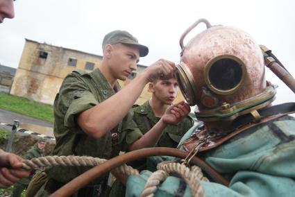 Солдат железнодорожных войск закрывает иллюминатор на тяжелом водолазном шлеме водолаза перед погружением