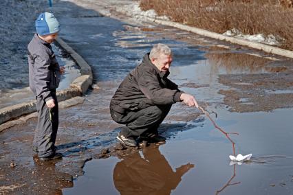 Дед с внуком пускают бумажный кораблик.