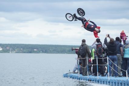 Прыжки на велосипедах в воду Bicycle live fest, парень в костюме супермена прыгает на велосипеде с трамплина