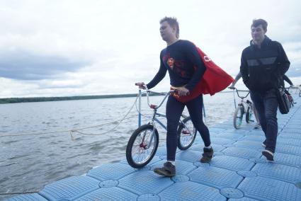 Прыжки на велосипедах в воду Bicycle live fest, парень в костюме супермена везет свой велосипед к трамплину