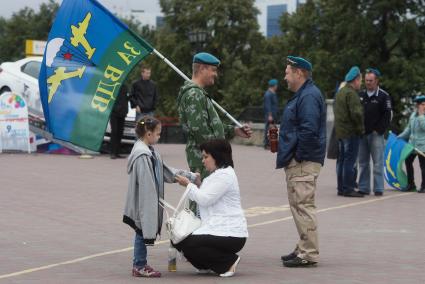 Десантники собираются на площади у памятника основателям города в ожидании сослуживцев. Женщина одевает отцовскую куртку на девочку