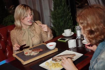 Девушки в ресторане  \"Огонек\" в Екатеринбурге, который ввел санкционное меню., едят \"скумбрия подкопченая и запеченая с ароматными дачными травами с отварным картофелем и сливочным маслом\" и  отбивную из говяжей вырезки с перлотто и клюквеным соусом