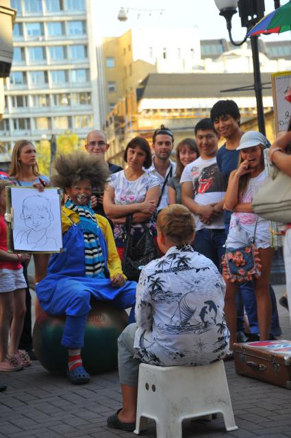 Улица Старый Арбат. На снимке:  художник в костюме клоуна рисует шаржи людей.