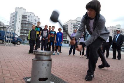 Мужчина в день физкультурника бьет кувалдой по наковальне силомера