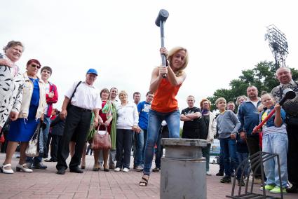 Девушка в день физкультурника бьет кувалдой по наковальне силомера