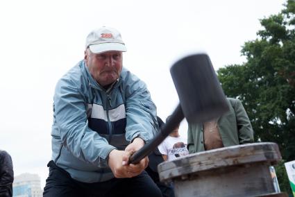 Мужчина в день физкультурника бьет кувалдой по наковальне силомера