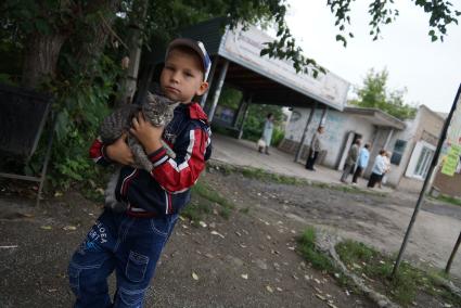 мальчик держит на руках кошку у остановки общественного транспорта в городе Ирбит