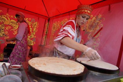 девушка с традиционном русском наряде печет блины на Ирбитской ярмарке