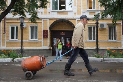 мужчина проходит с тележкой с металлическим бидон мимо здания администрации в городе Ирбит