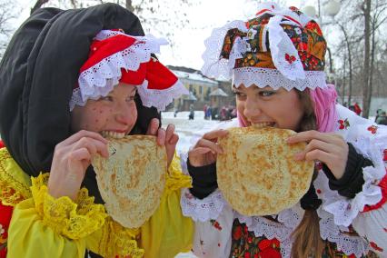 Девушки едят блины на масленнице.